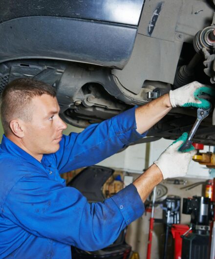 car mechanic worker repairing suspension of lifted automobile at auto repair garage shop station